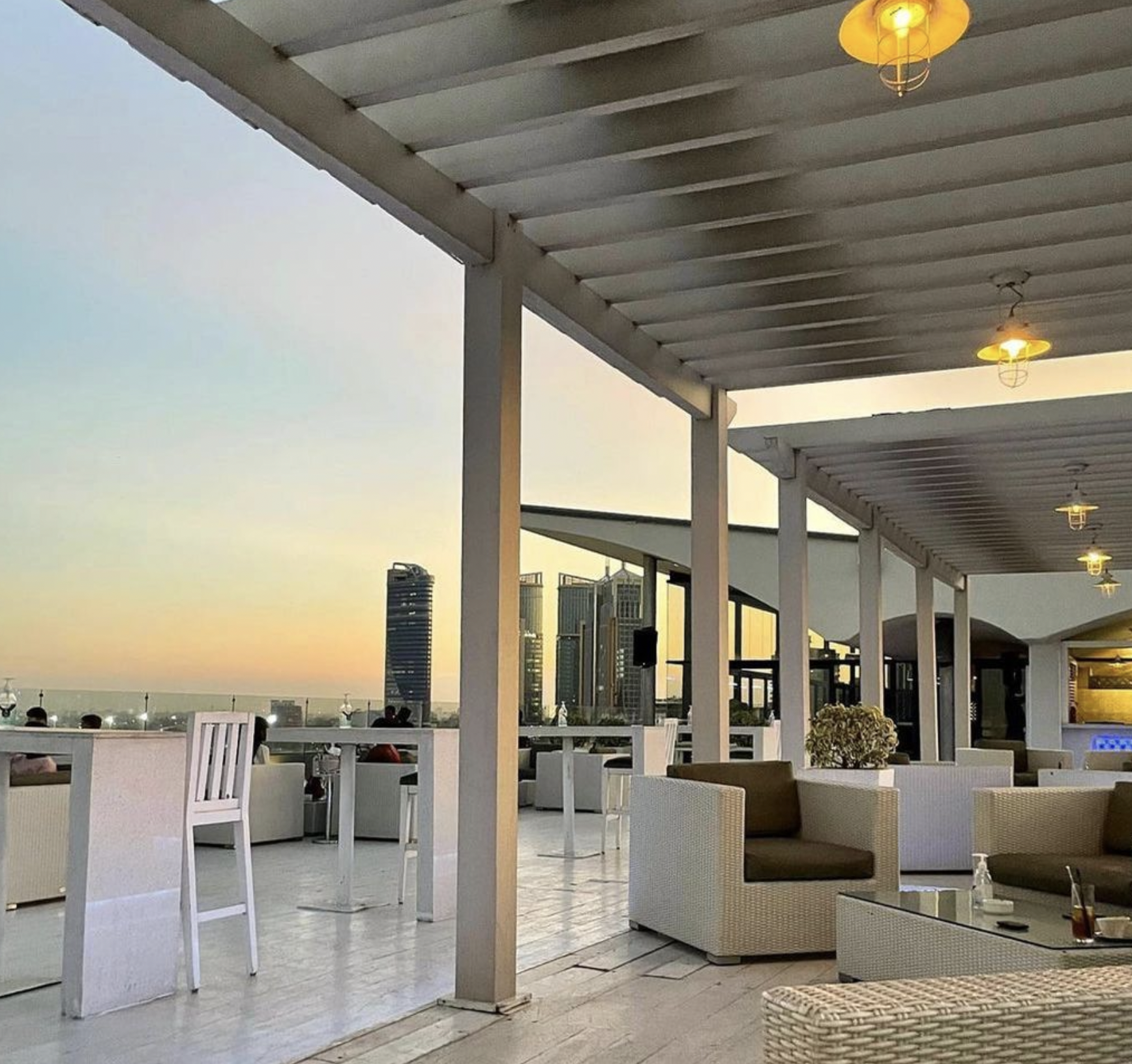 There is an empty lounge in the foreground. In the background is the cityscape of Dar es Salaam and the sunset is coloring the sky a light orange.