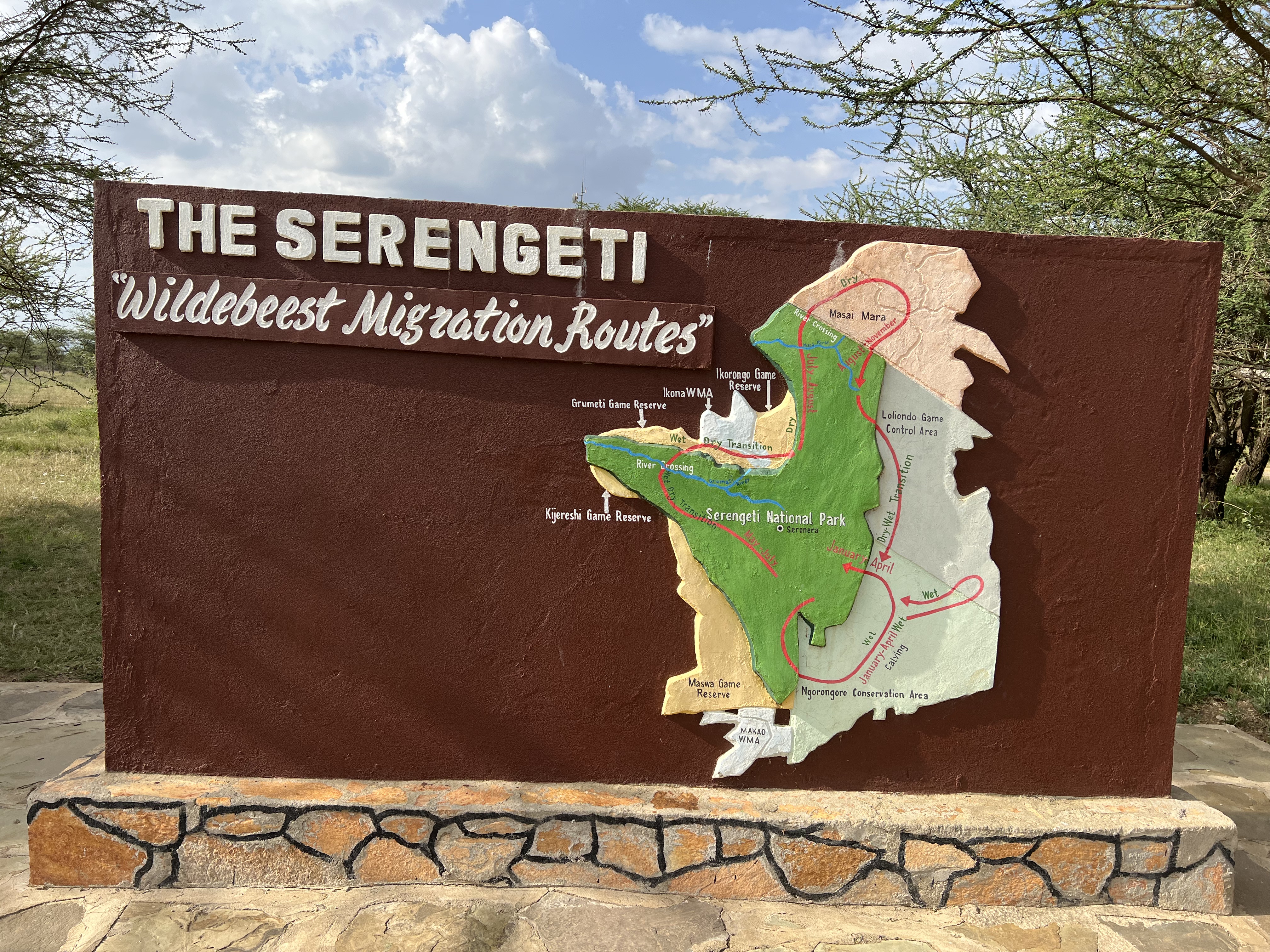 A sign that reads 'The Serengeti Wildabeast Migration Routes' and has a map that depicts the path of the migration.