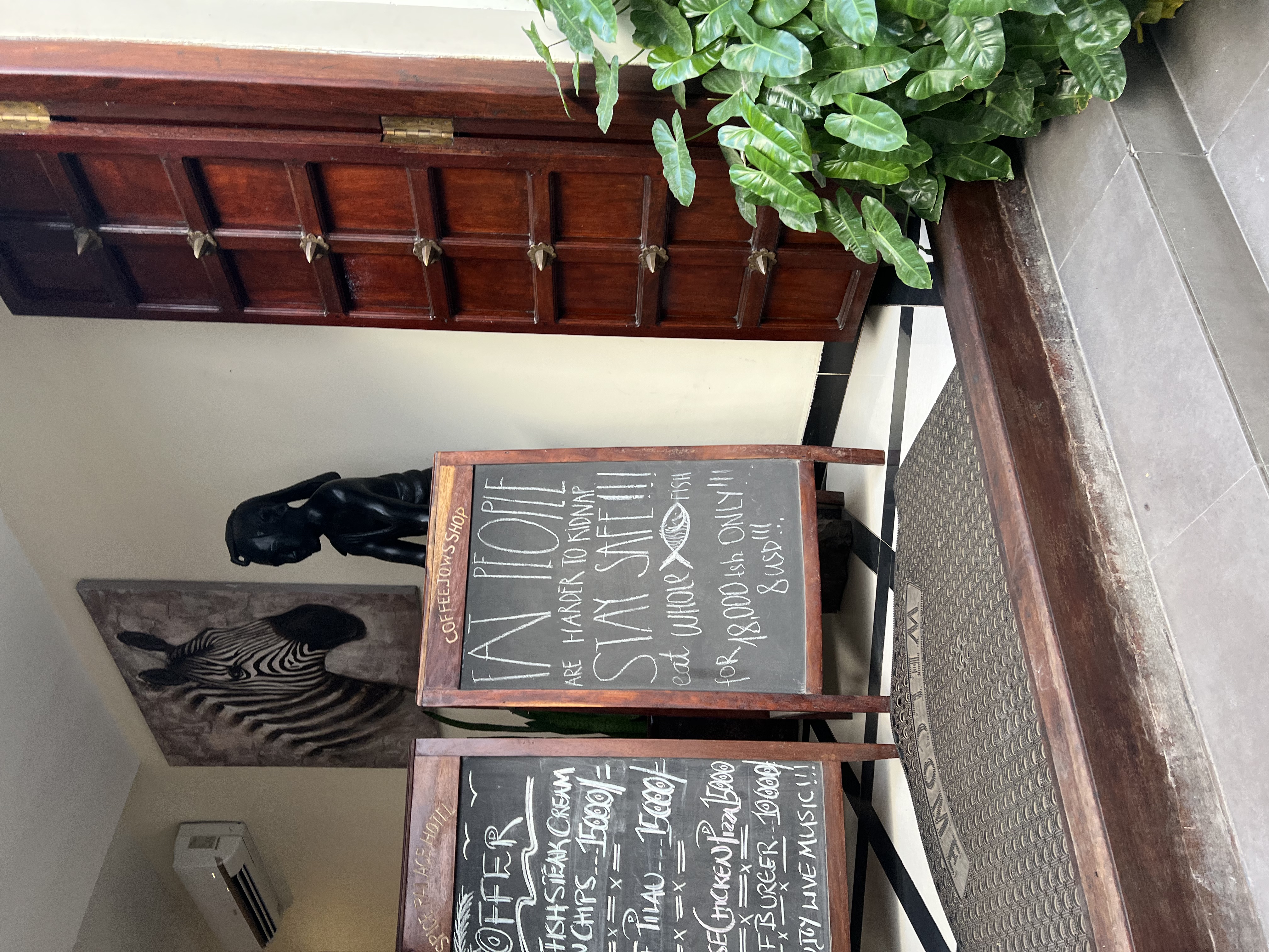 A coffee shop in Stone Town with a traditional door that is opened. At the entrance of the shop there is a sign that reads 'Fat People are Harder to Kidnap. Stay Safe!'